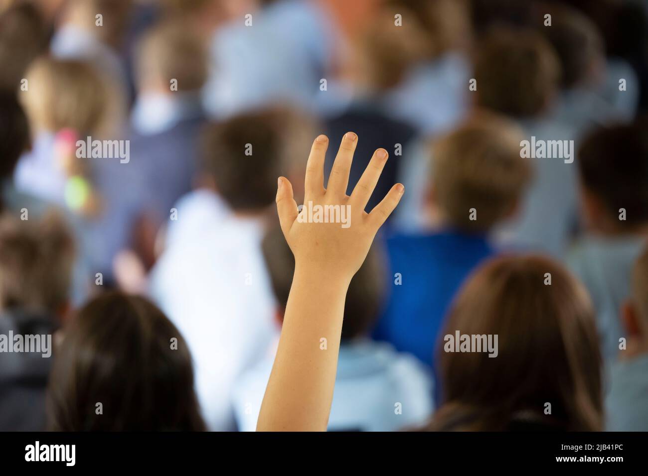 Un niño levanta su mano en el aire durante una lección en un salón de clase escolar. Foto de stock