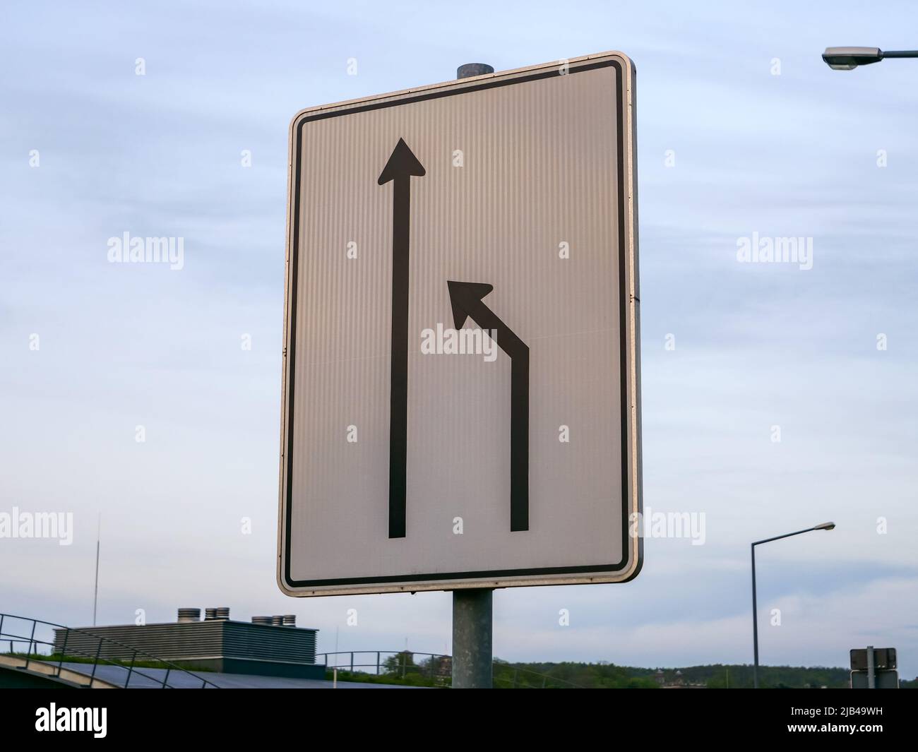 Incorpórese a la izquierda en la señal de tráfico de Alemania. El carril derecho termina y los conductores de coches deben cambiar al carril izquierdo. Señal de carretera con flechas. Foto de stock