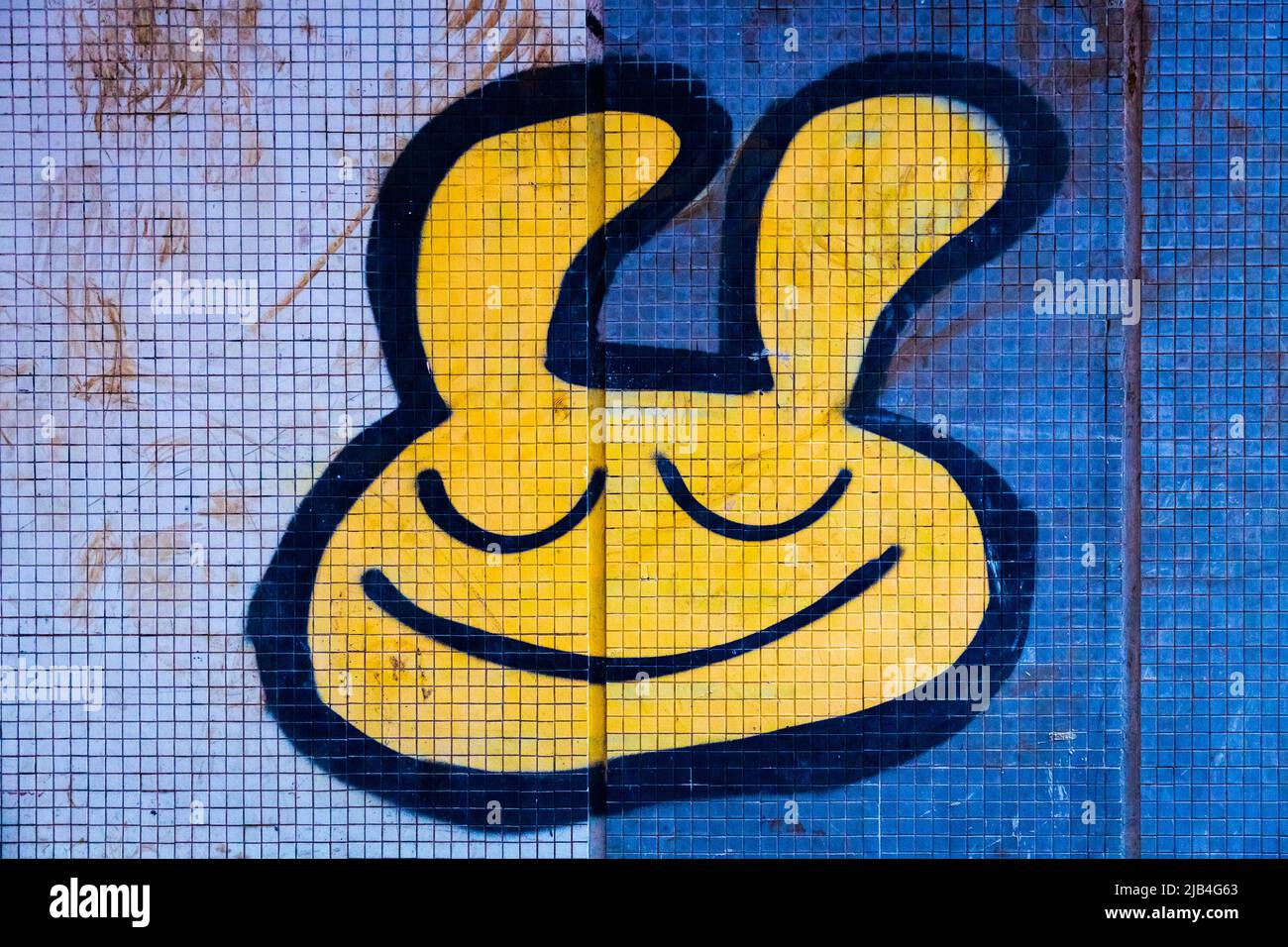 Graffiti amarillo sonriente dibujos animados pintadas de forma esprayada arte callejero con los ojos cerrados. Foto de stock