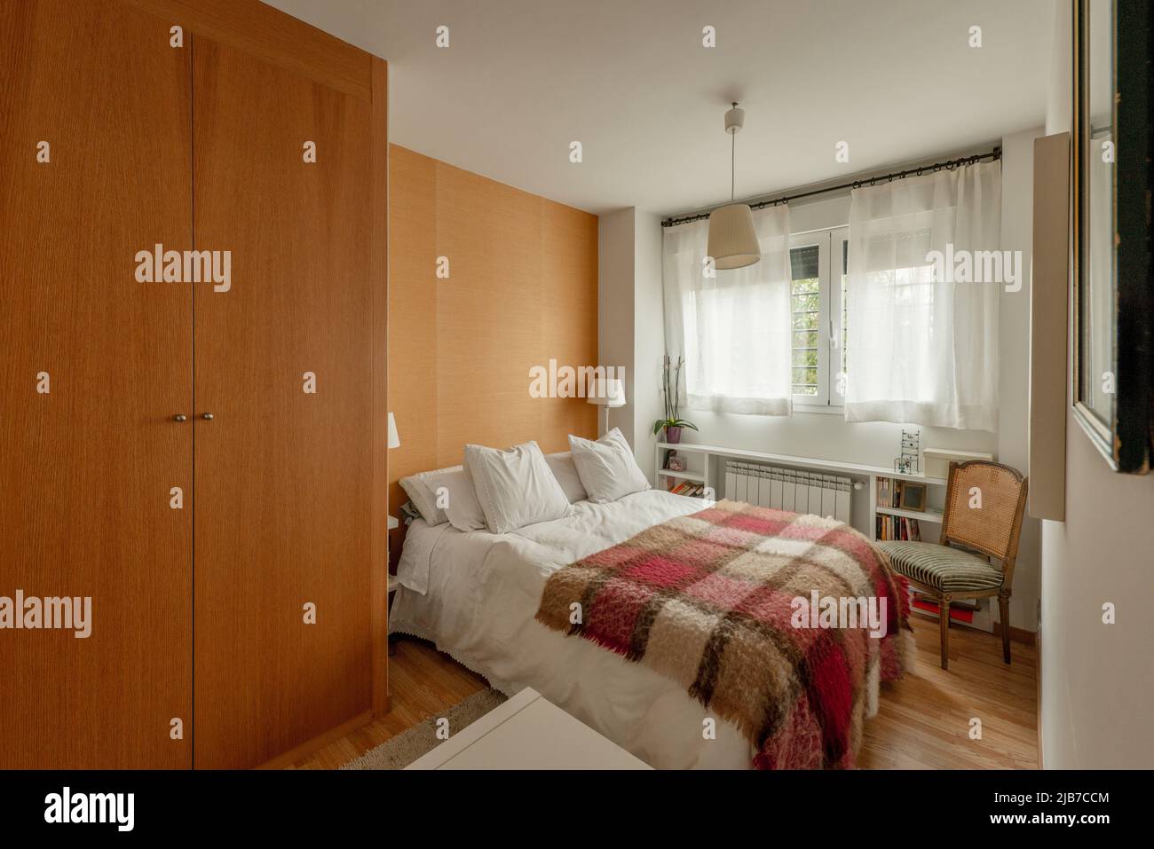 Habitación doble con armario de cerezo claro, cama con edredón blanco y  manta a cuadros Fotografía de stock - Alamy
