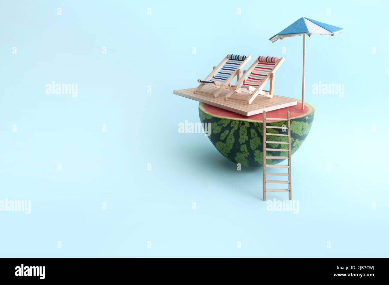 Sandía de verano con sombrilla, dos tumbonas y escalera de madera en la playa Foto de stock