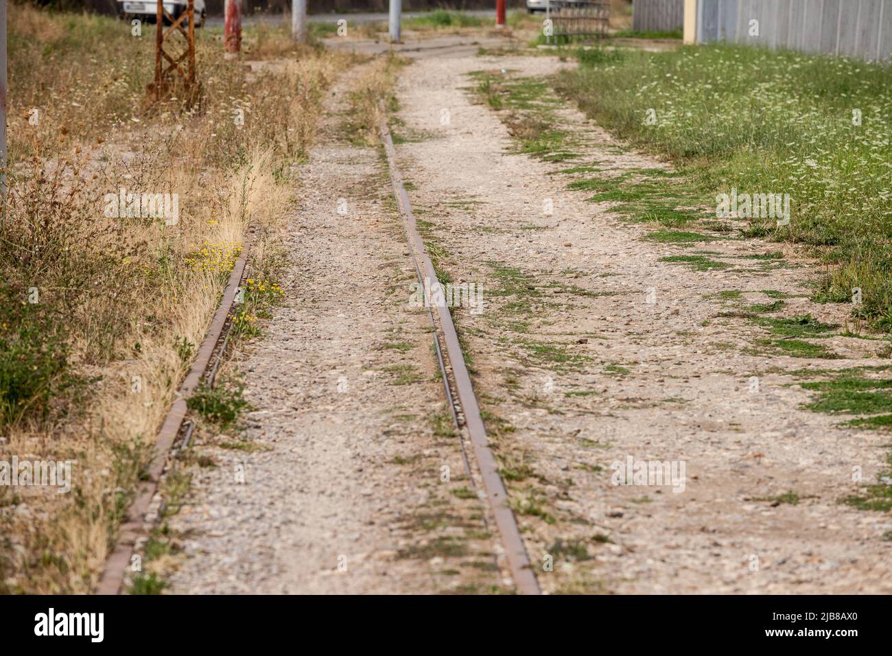 Imagen de una vía de tren abandonada con sus líneas férreas oxidadas con perspectiva, cubiertas de hierba y barro. Foto de stock