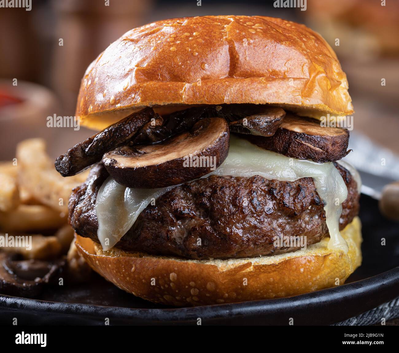 Cierre de una hamburguesa de champiñones en un trasero tostado con patatas fritas en un plato negro Foto de stock