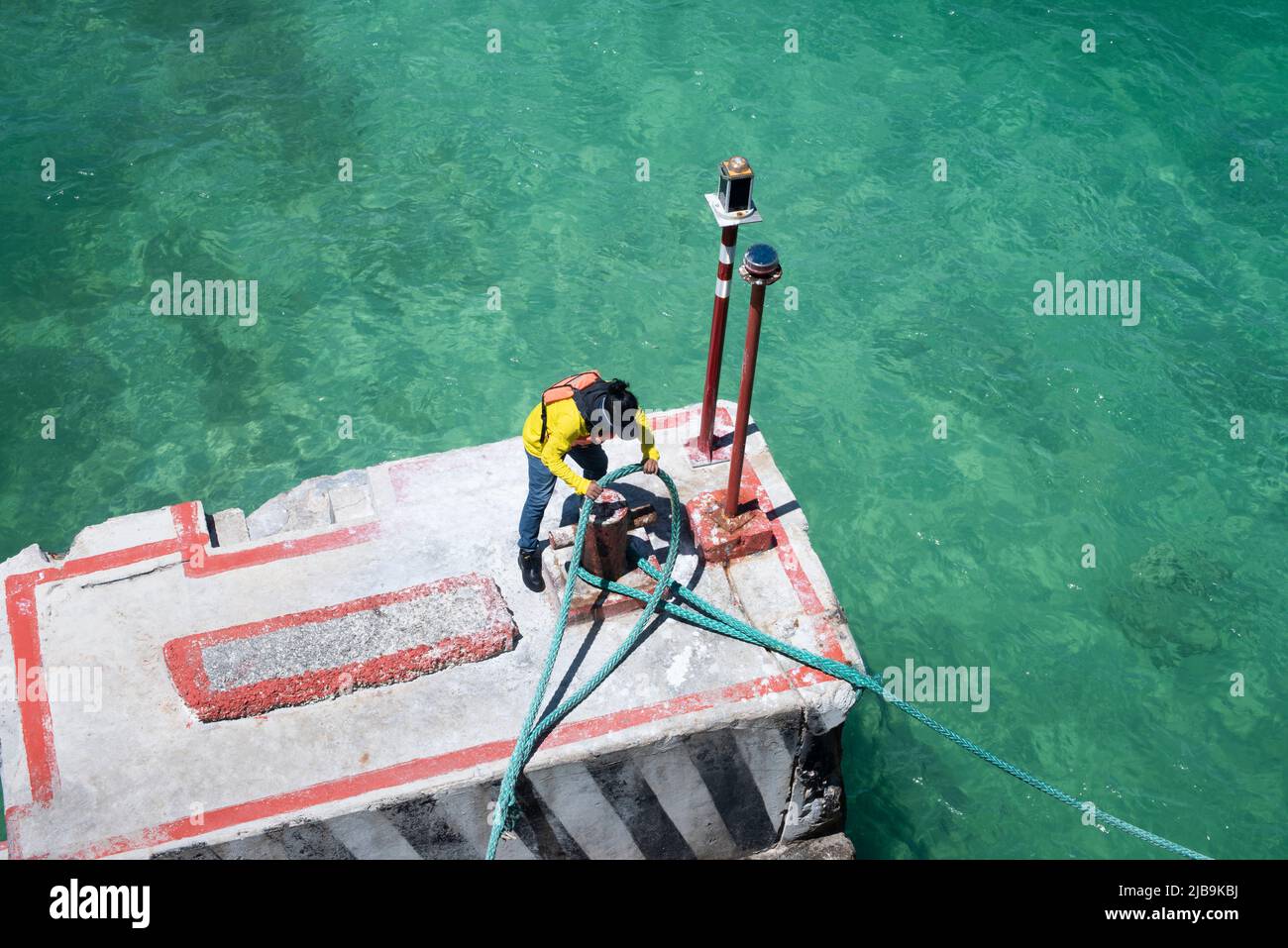 Un trabajador del muelle tira de cuerdas a un barco, envuelto alrededor de una bollard amarre en un muelle en el puerto. Foto de stock