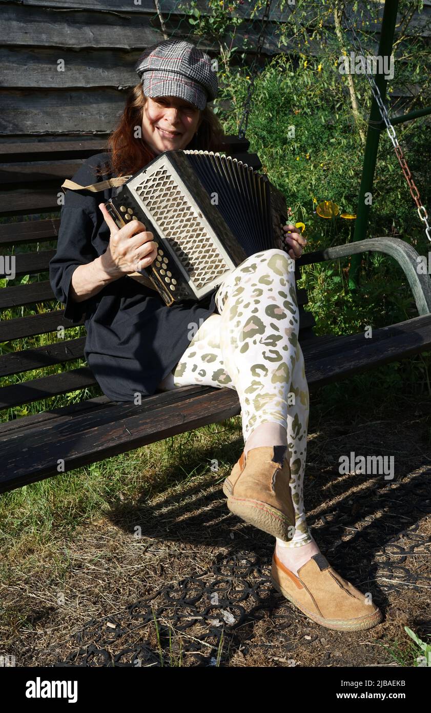 Mujer pelirroja sentada en un banco y jugando un acordeón de botón diatónico Foto de stock