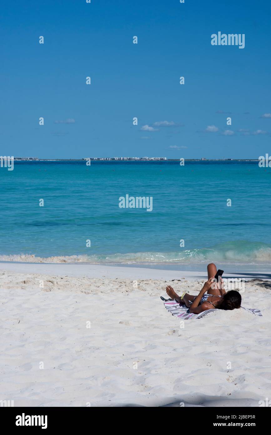 Una mujer joven de vacaciones tumbada en una playa de una isla tropical usando un smartphone Foto de stock