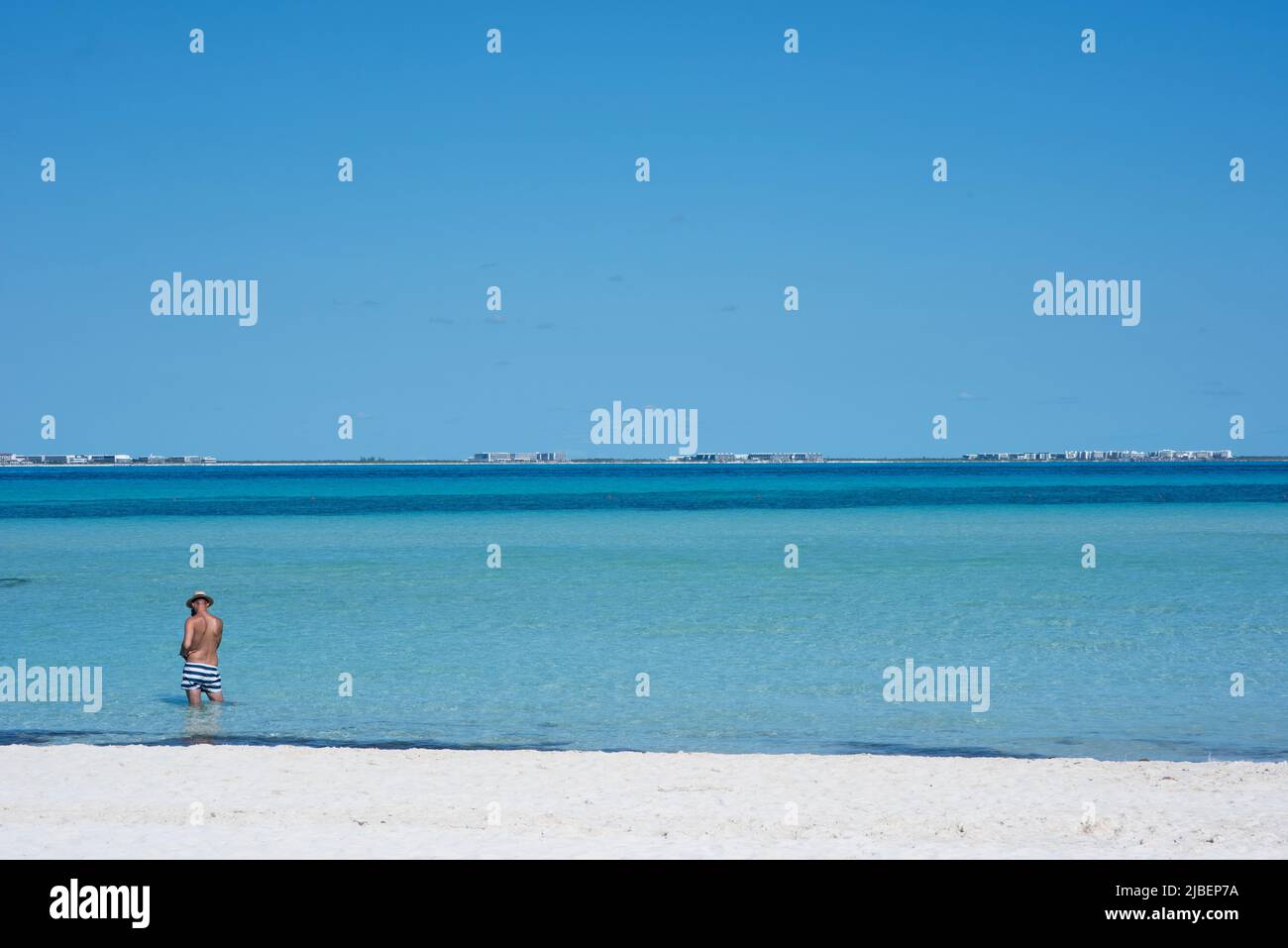 Vista trasera de un hombre parado en la playa en un traje de baño observando el horizonte sobre el Mar Caribe Foto de stock