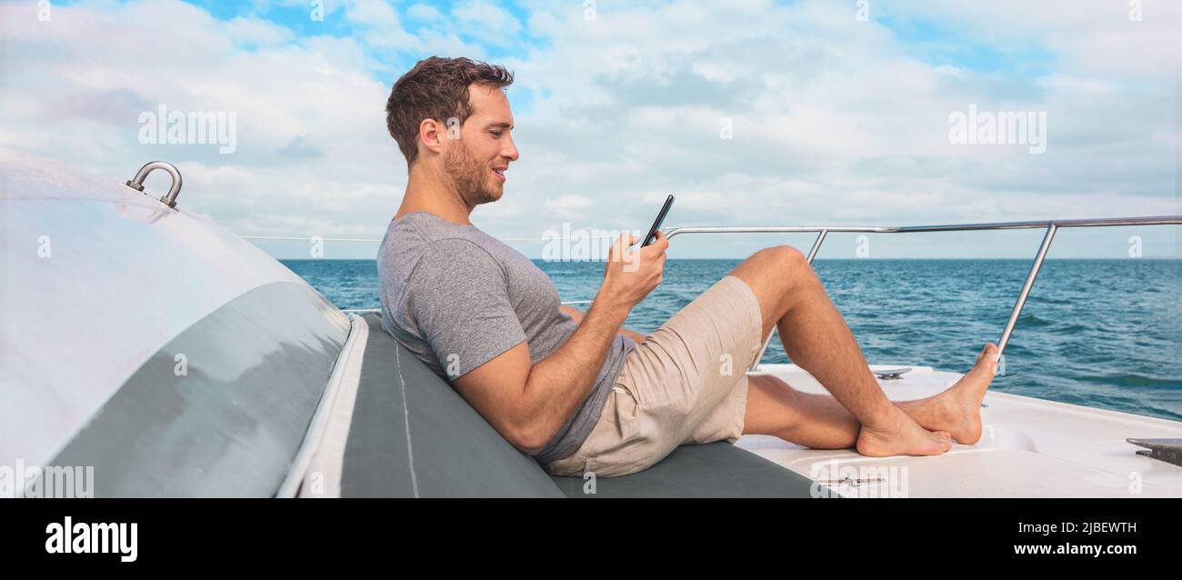 Teléfono que utiliza en el crucero. Hombre viajes de lujo mensajes de texto con datos en el barco de yates relajarse en la bandera de la cubierta panorámica. Vacaciones en el Caribe Foto de stock