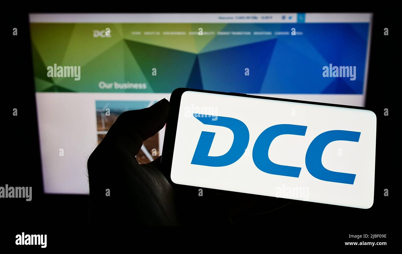 Persona con smartphone con el logotipo de la empresa irlandesa de ventas y marketing DCC plc en la pantalla delante del sitio web. Enfoque en la pantalla del teléfono. Foto de stock