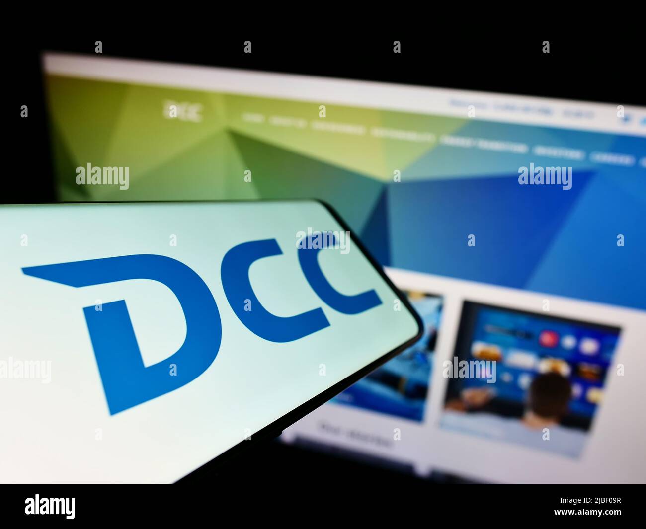 Smartphone con el logotipo de la empresa irlandesa de ventas y marketing DCC plc en la pantalla frente al sitio web de la empresa. Enfoque en la parte central izquierda de la pantalla del teléfono. Foto de stock