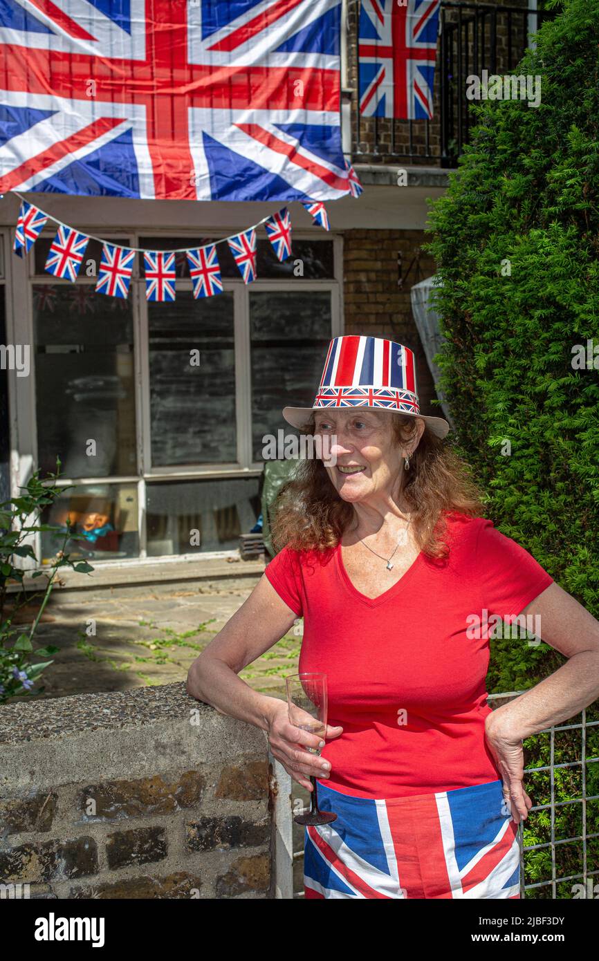 Mujer frente a las banderas de Union Jack y amontándose en una casa del consejo en Londres para celebrar los 70 años del reinado de Su Majestad la Reina. Foto de stock