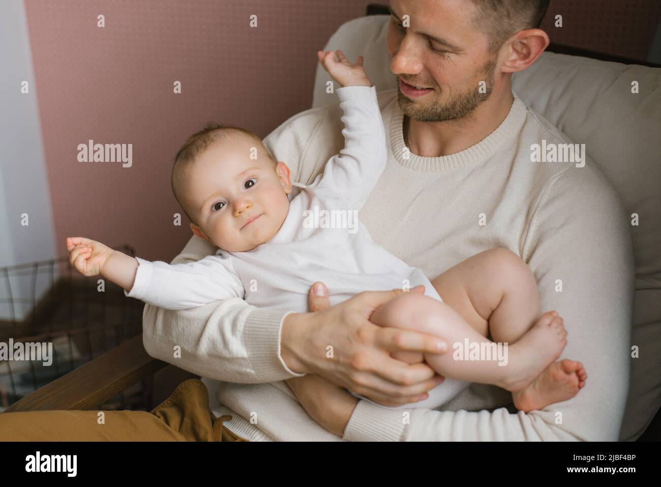 Un bebé sonriente en los brazos de su joven padre feliz Foto de stock