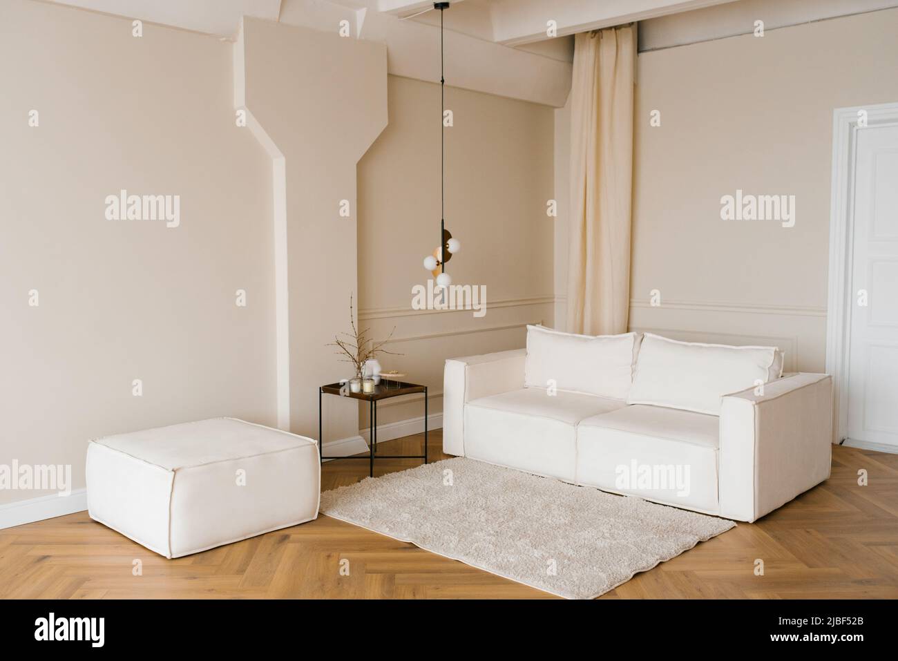 El interior escandinavo tiene un sofá luminoso en el suelo de parqué, una mesa lateral de madera y paredes de color beige Foto de stock