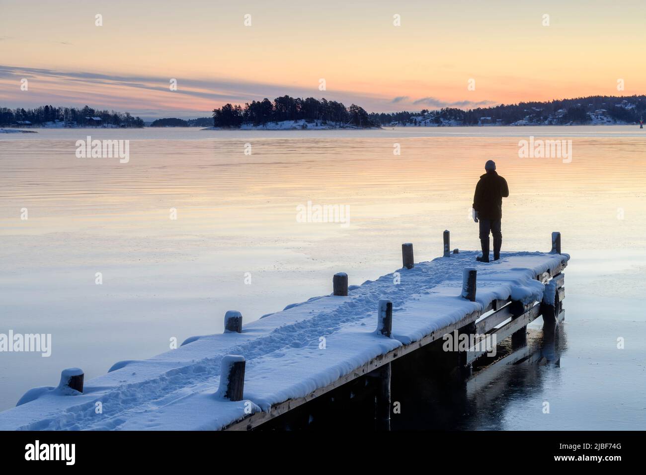 Hombre en un embarcadero nevado en el lago al atardecer Foto de stock