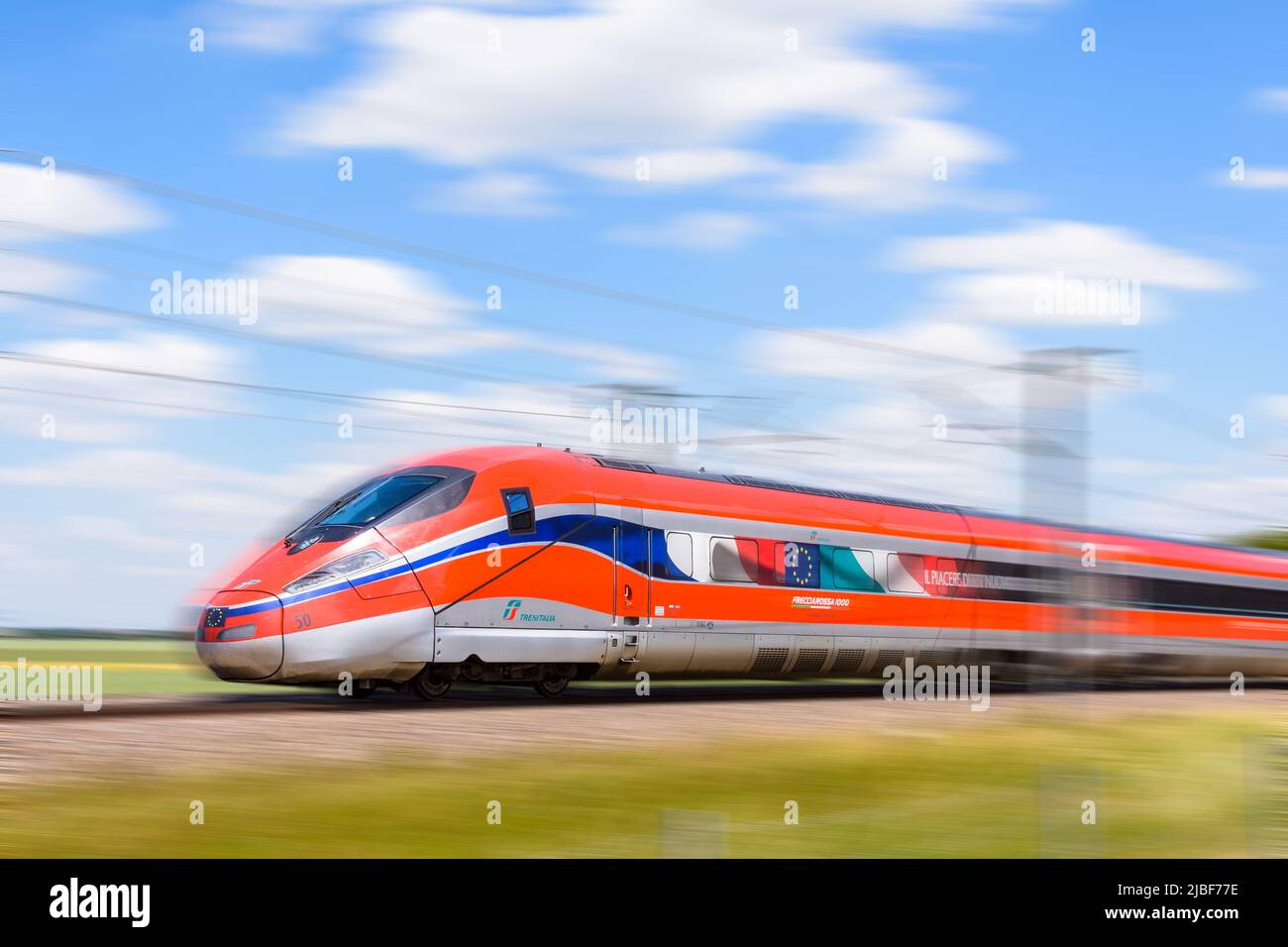 Un tren de alta velocidad Frecciarossa (ETR 1000) de la compañía ferroviaria italiana Trenitalia conduce a toda velocidad en el campo. Foto de stock