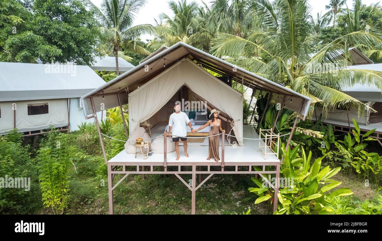 joven pareja de turistas de pie frente a una tienda de camping de lujo en una selva tropical Foto de stock