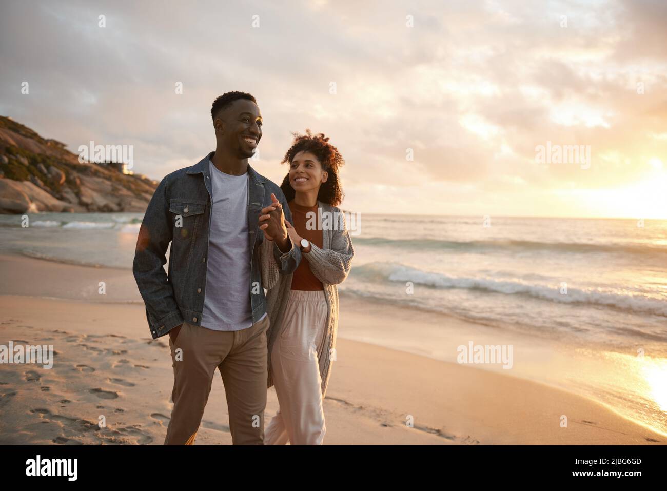 Sonriendo joven pareja multiétnica caminando a lo largo de una playa al atardecer Foto de stock