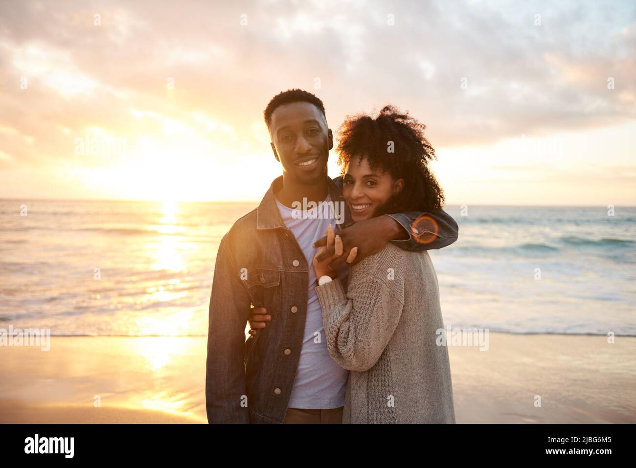 Amante joven pareja multiétnica sonriendo en la playa al atardecer Foto de stock