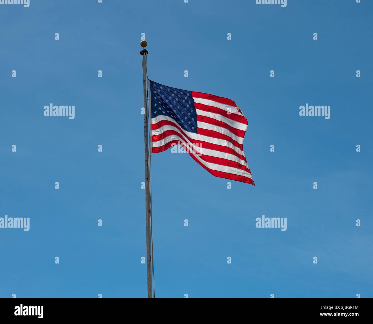 Una bandera azul y blanca brillante de América ondeando en un fondo azul claro del cielo Foto de stock