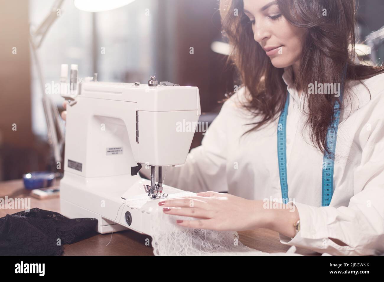 Vista de cerca de la máquina de coser y la joven mujer a medida trabajando en ella mientras está sentado en un taller. Foto de stock