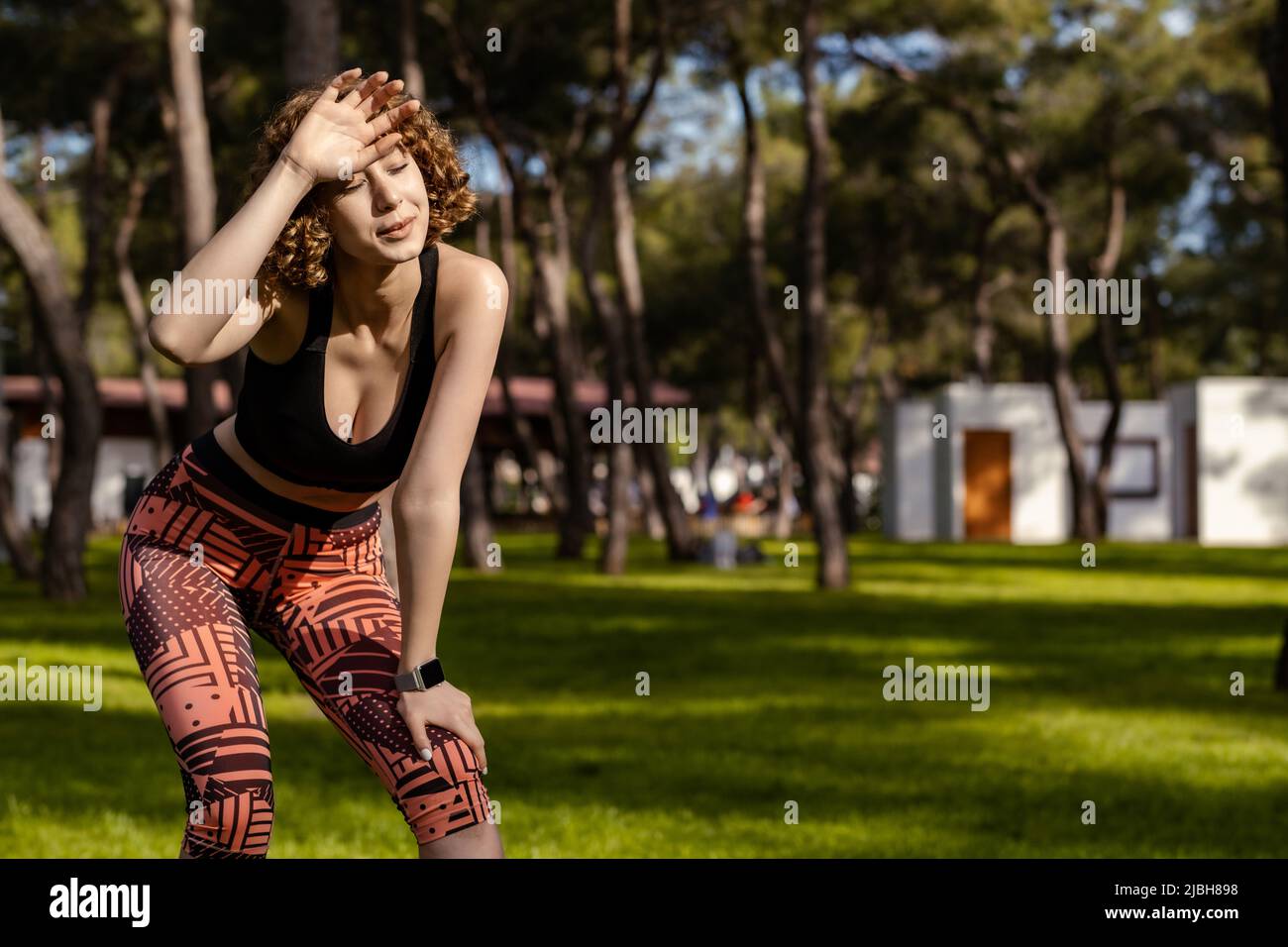 Mujer joven hermosa que usa ropa deportiva en el parque de la ciudad, al  aire libre después de correr atrapando su aliento, limpiando su sudor de su  frente Fotografía de stock -