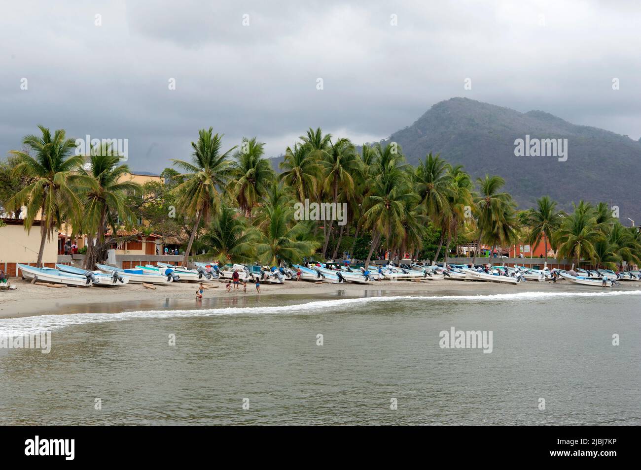 Vista panorámica de barcos de pesca en la playa con palmeras y colinas en Zihuatanejo, México Foto de stock