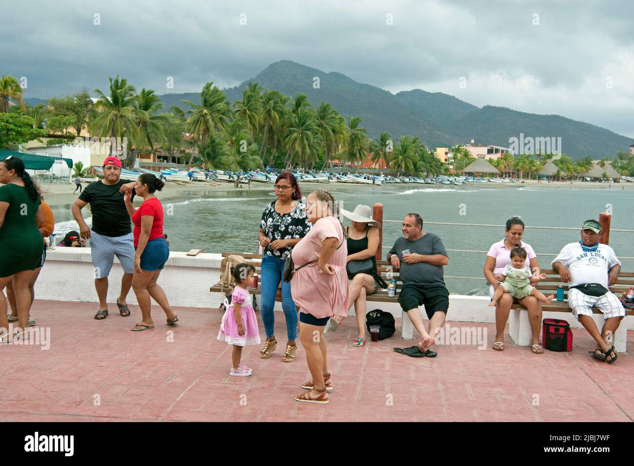 Gente en el muelle escuchando música en vivo con vistas panorámicas de la playa con barcos de pesca en Zihuatanejo, México Foto de stock