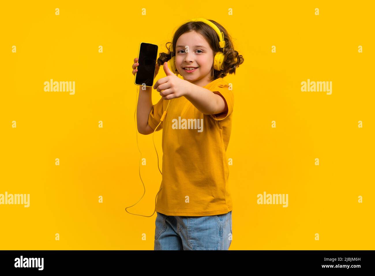 Chica sin preocupaciones con ropa amarilla muestra el pulgar sobre fondo  amarillo. Colegiala con canciones, podcast, audiolibros en el teléfono  celular. Escucha música con la cabeza Fotografía de stock - Alamy