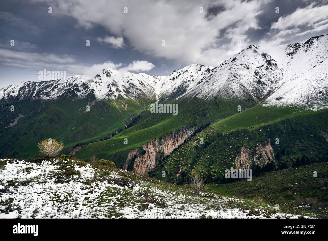 Paisaje de valle nevado con verdes colinas sobre cielo nublado en Kazajstán Foto de stock
