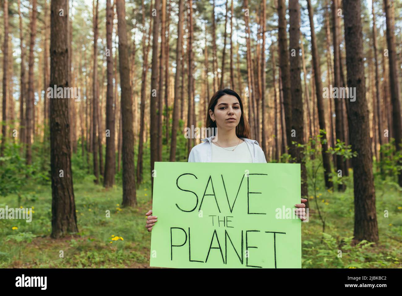 Joven activista de pie en el bosque con un cartel salvar el planeta, una voluntaria lucha con la deforestación Foto de stock