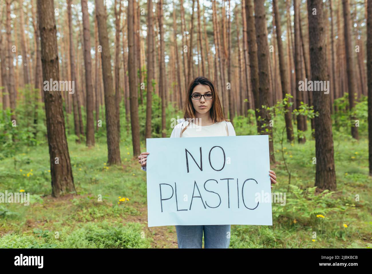Joven activista de pie en el bosque sin cartel plástico, voluntaria luchando con la contaminación del bosque Foto de stock