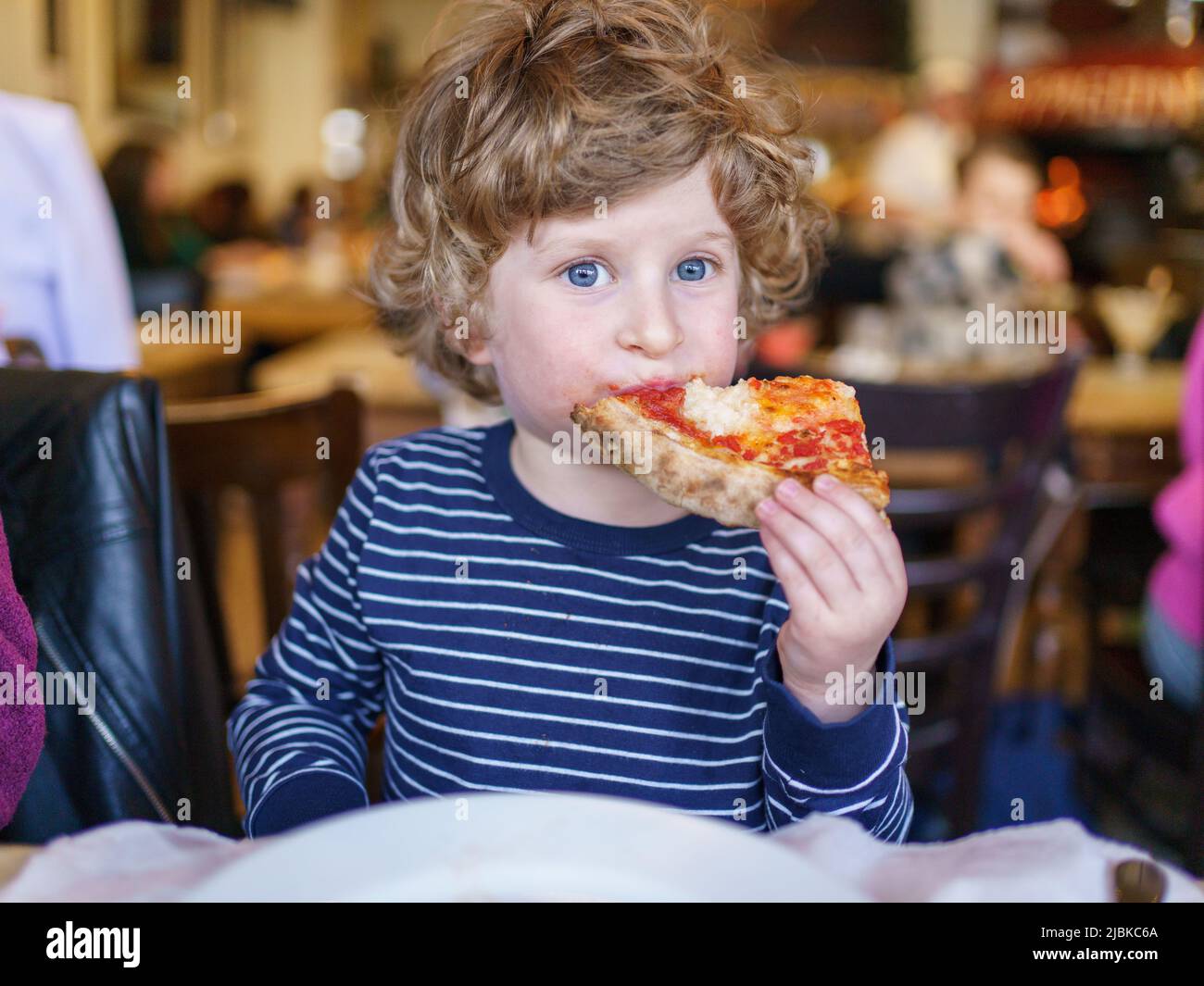 Niño de tres años comiendo pizza rebanada en el restaurante italiano, Reino Unido Foto de stock