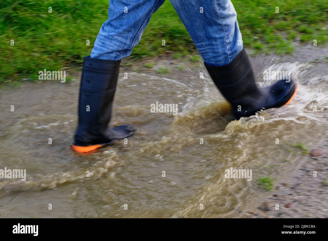 Las botas de agua mantienen los pies secos mientras que salpican a través de un charco fangoso Foto de stock