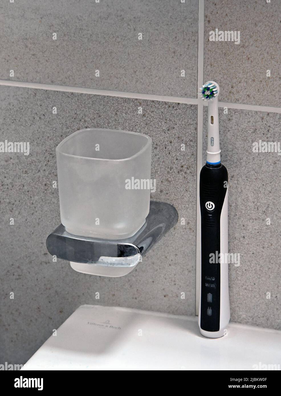 Cepillo dental eléctrico Oral B y vidrio de agua en el baño de azulejos. Foto de stock