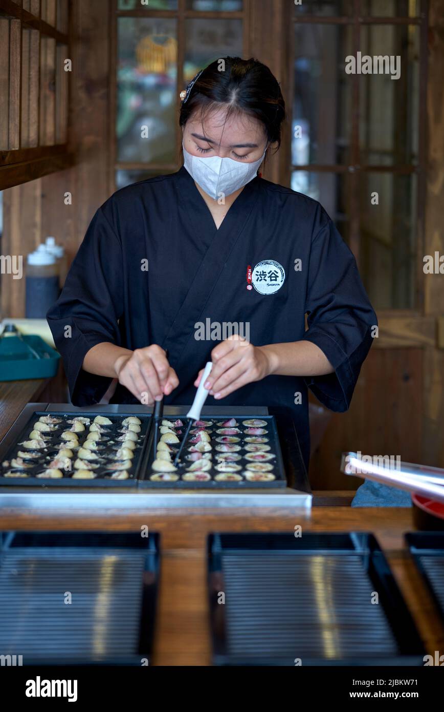 Chef mujer en un restaurante japonés que cocina los dumplings tradicionales japoneses de Takoyaki Foto de stock