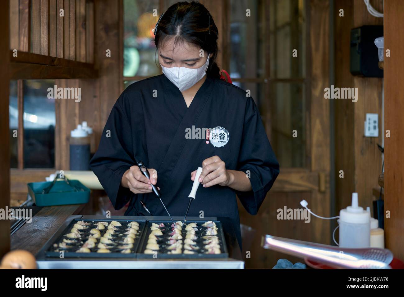 Chef mujer en un restaurante japonés que cocina los dumplings tradicionales japoneses de Takoyaki Foto de stock