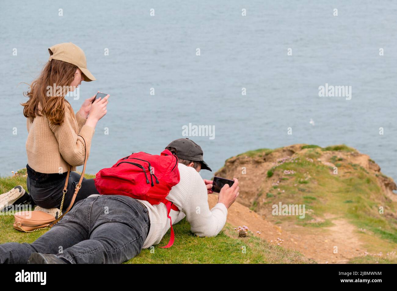 Padre e hija observando aves y fotografiando la naturaleza, tumbados en la cima de los acantilados costeros Foto de stock