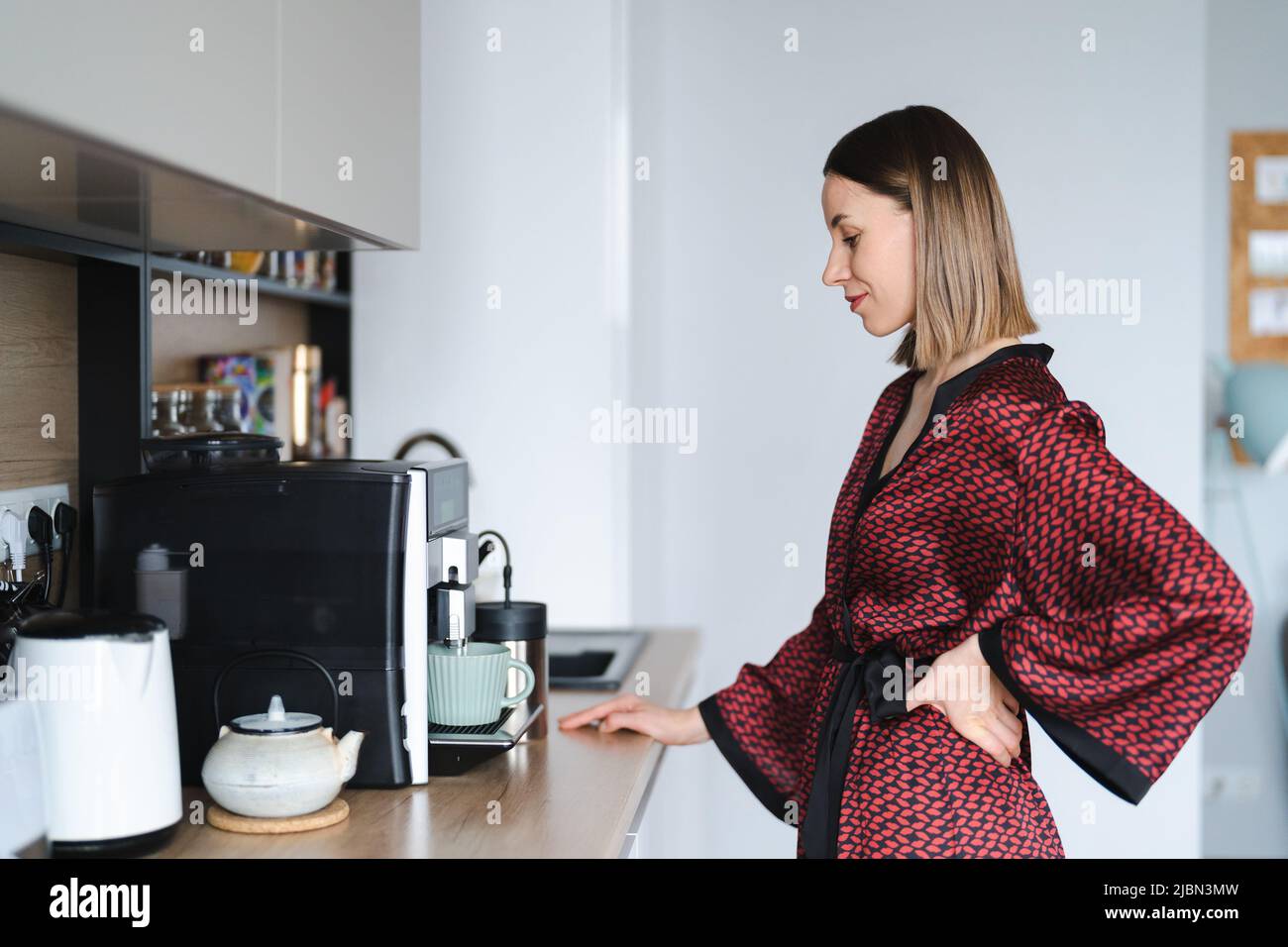 Mujer que usa la cafetera para hacer una taza de café grande en casa. Mujer  que usa bata de seda en casa mientras prepara un latte Fotografía de stock  - Alamy