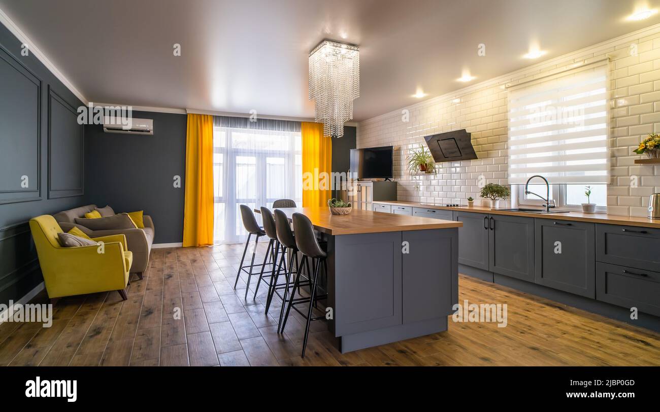 Interior de cocina moderna en azul con detalles amarillos y suelo de madera con una gran mesa en el medio de la habitación, zona de cocina y sofá para relajarse Fotografía de Interior de cocina moderna en azul con detalles amarillos y suelo de madera con una gran mesa en el medio de la habitación, zona de cocina y sofá para relajarse Fotografía de