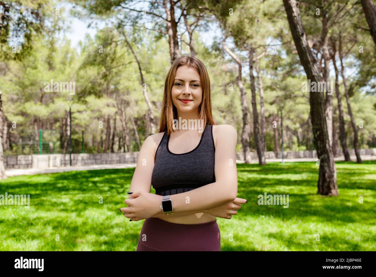 Hermosa mujer morena con sujetador deportivo de pie en el parque de la ciudad, al aire libre Feliz cara sonriendo con los brazos cruzados mirando hacia fuera con confianza expressio Foto de stock