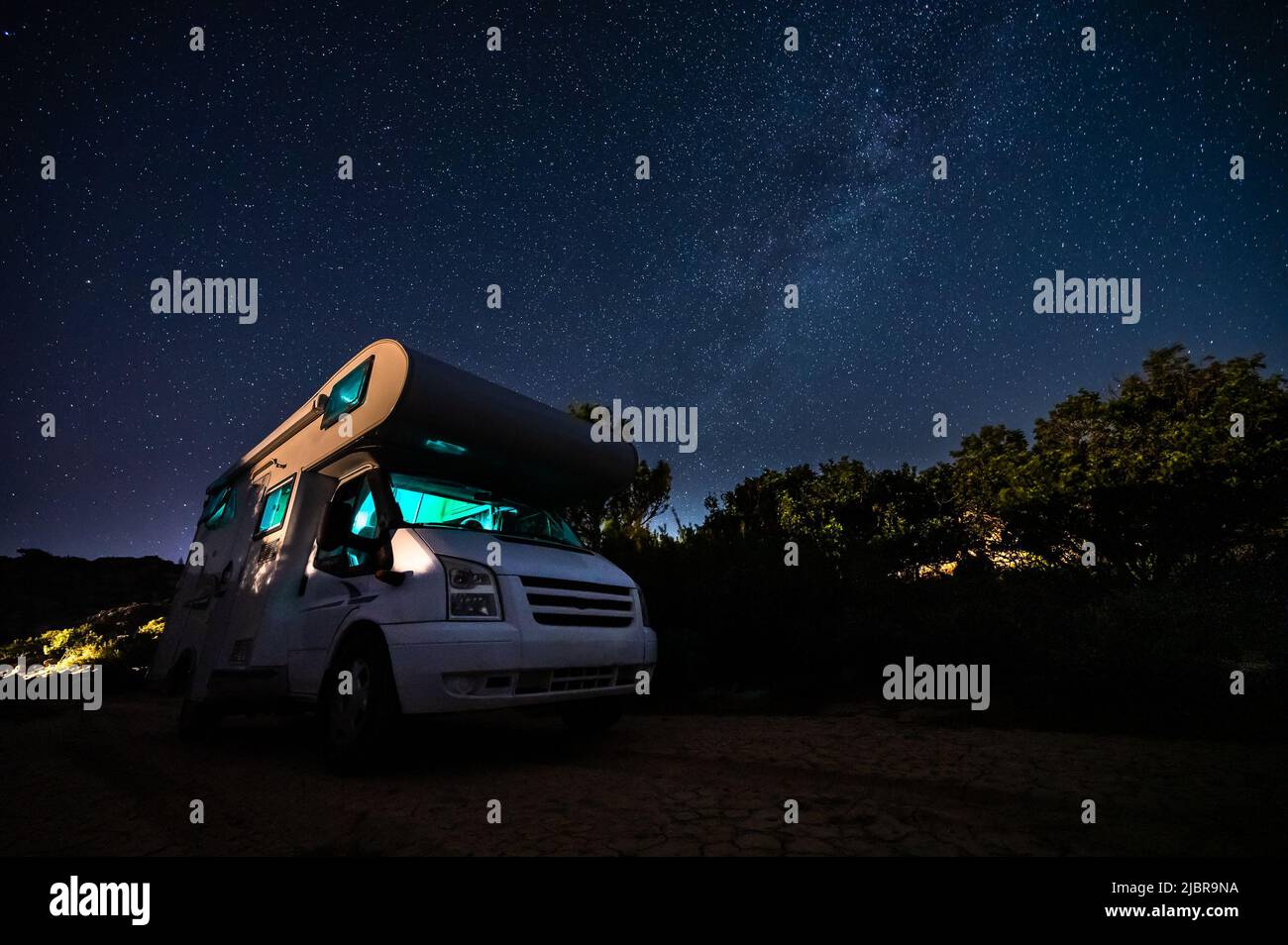 Autocaravana estacionada bajo estrellas en un muelle junto al mar, Creta, Grecia. Los viajeros con camioneta descansan durante la noche bajo la forma lechosa en una familia activa Foto de stock