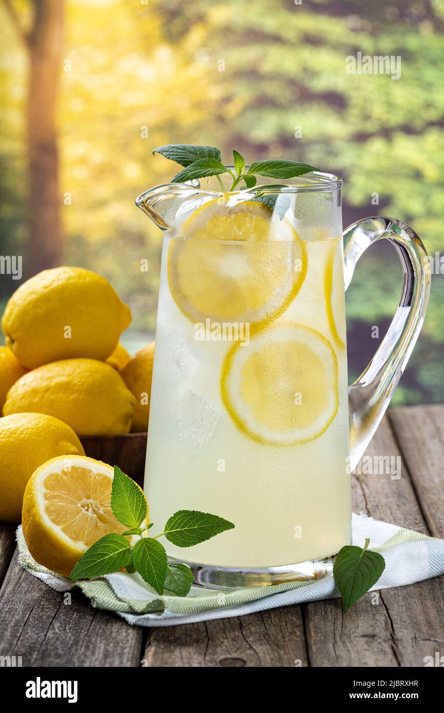 Jarra de limonada con rodajas de limón y menta sobre una vieja mesa de madera con fondo rural de verano Foto de stock