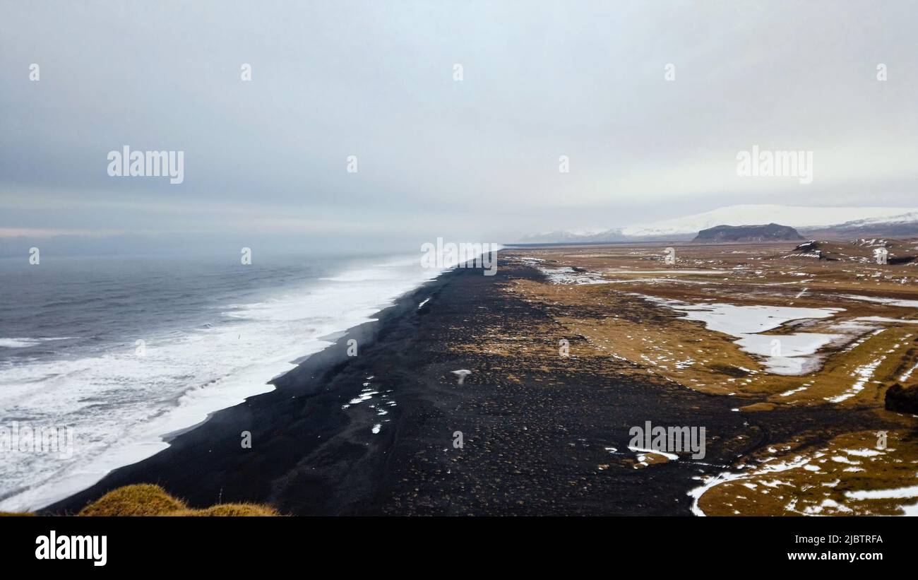 Vista desde el faro de Dyrholaey, en Islandia, con vistas a la playa de arena negra que se encuentra debajo durante el invierno, con nieve y un hermoso clima soleado. Foto de stock
