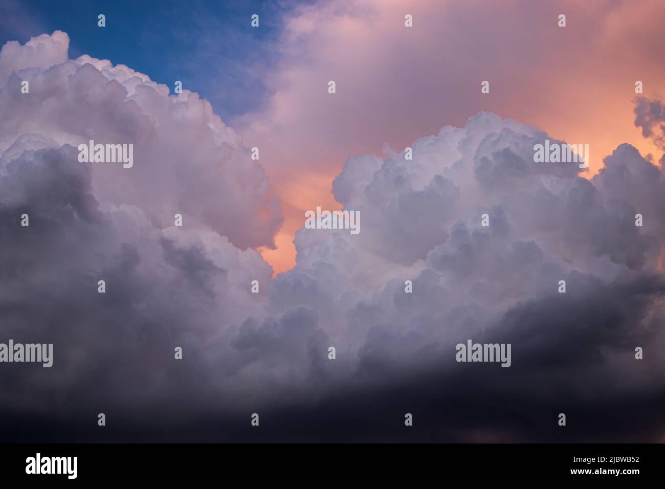 Espectaculares y detalladas nubes cúmulos apilados en un cielo azul con luz dorada y naranja del sol que se muestra a través Foto de stock