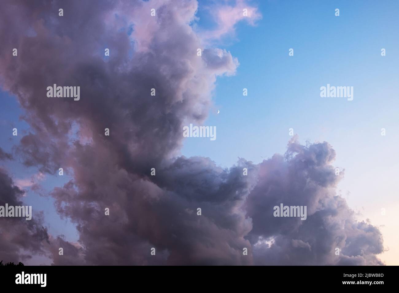 Espectaculares y detalladas nubes cúmulos apilados en un cielo azul con luz dorada y naranja del sol que se muestra a través Foto de stock