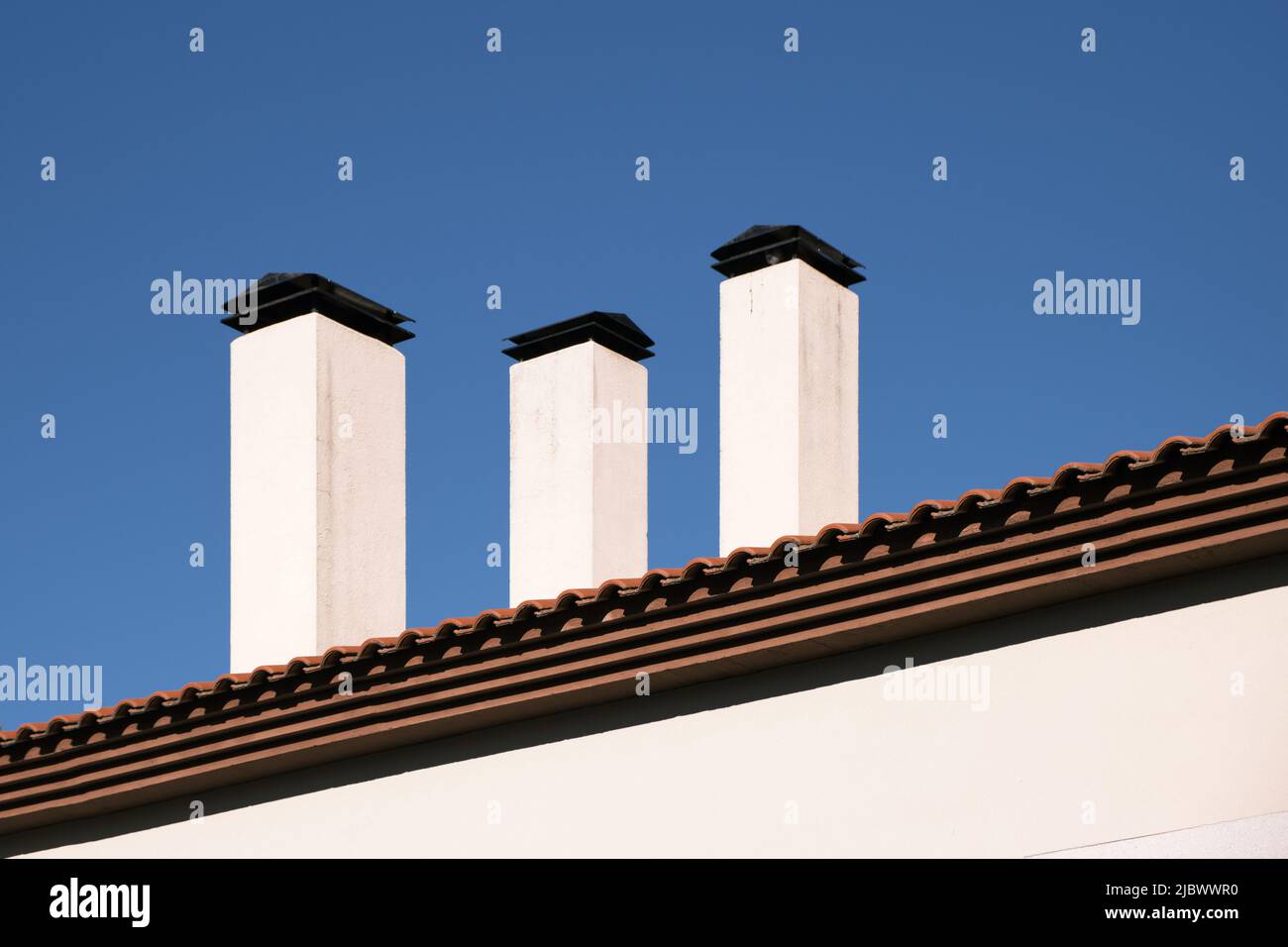 Primer plano de una azotea de una casa de campo con tres chimeneas blancas  contra el cielo azul Fotografía de stock - Alamy