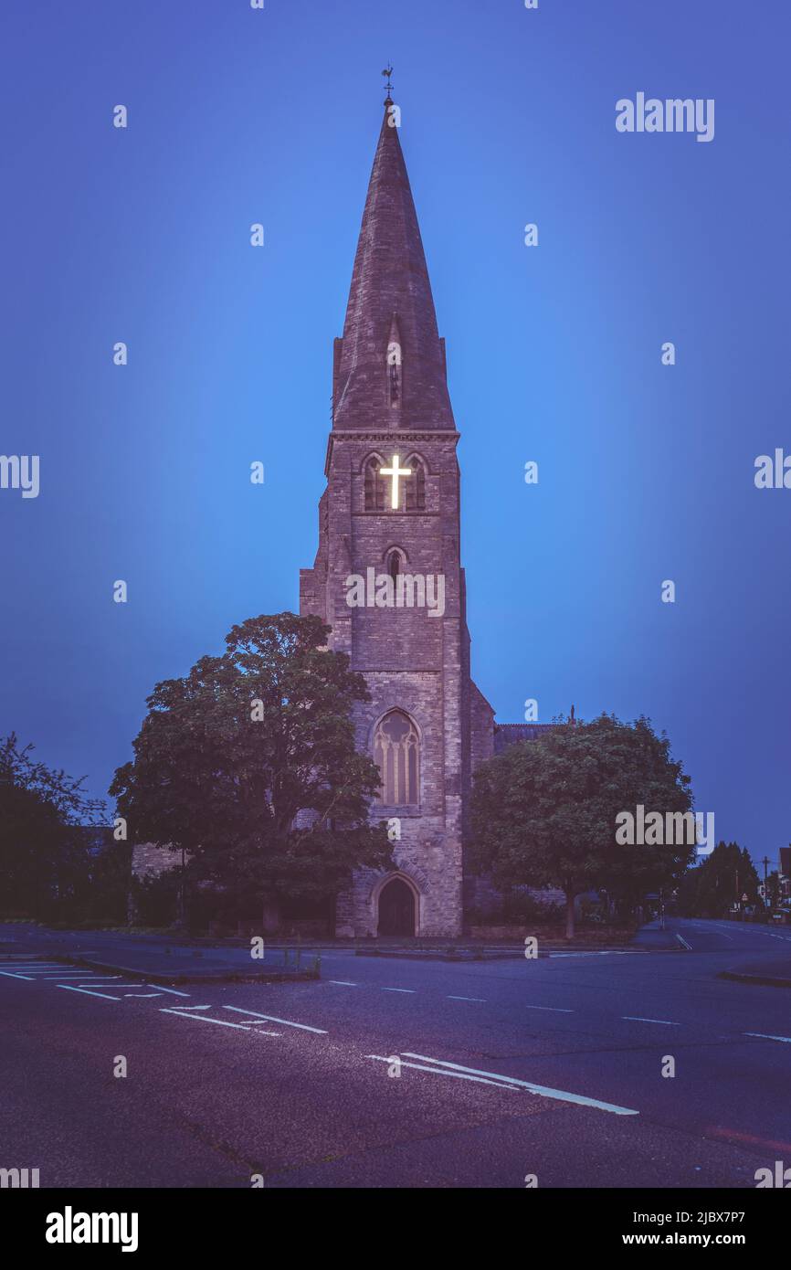 Edificio alto de la iglesia con cruz iluminada en la hora azul del atardecer, Inglaterra, Reino Unido Foto de stock
