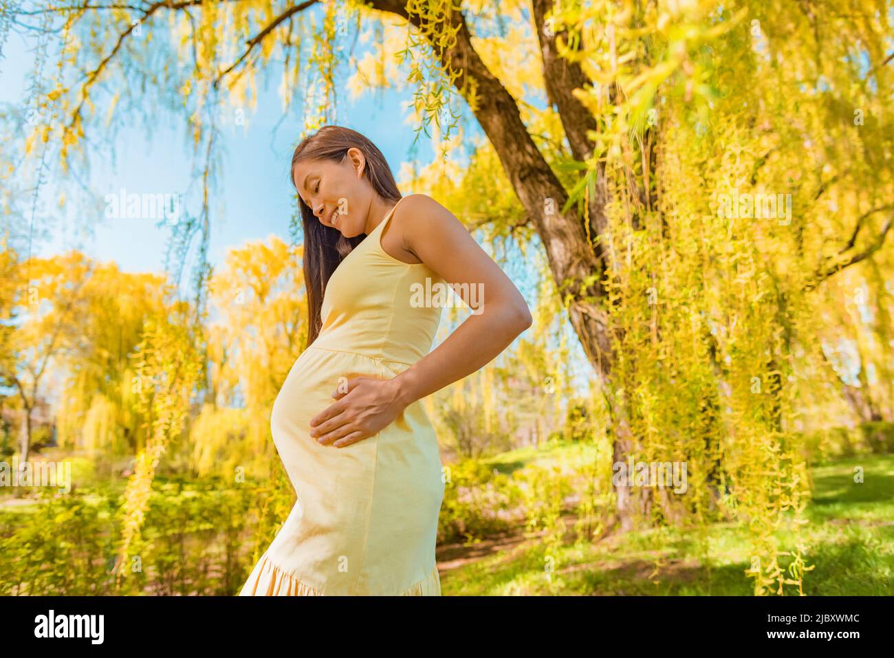 Maternidad ropa embarazo mujer embarazada asiática sosteniendo bebé protuberancia vientre caminando fuera en bosque naturaleza árboles amarillos con cómodo orgánico Foto de stock
