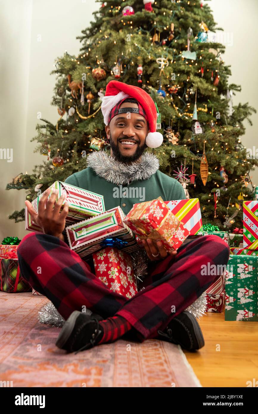 Feliz hombre afroamericano mirando a la cámara sonriendo con un montón de regalos envueltos en su regazo. Foto de stock