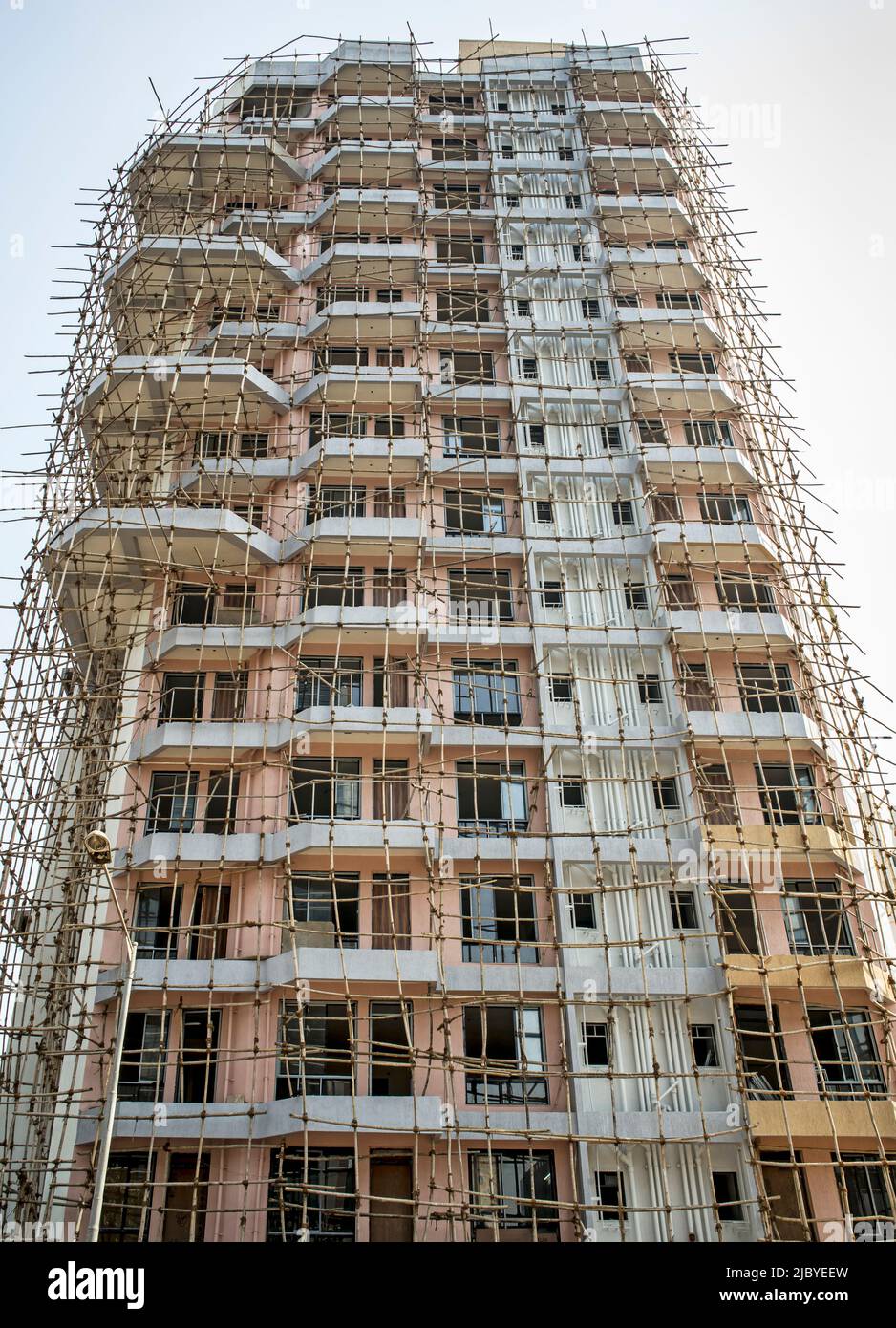 Edificio moderno de gran altura en construcción rodeado de andamios de bambú Foto de stock